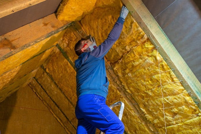 Man in mask putting up fiberglass insulation in attic.